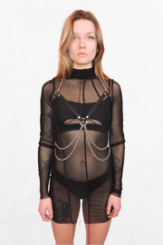 Model wearing a black webbing harness with silver metal accents. Thick adjustable straps wrap around the chest and waist, secured with silver buckles and O-rings. A bold statement piece for festivals, raves, and alternative fashion looks.