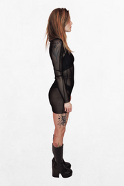  Model wearing a black mesh mini dress that fits snugly against the body. The sheer fabric reveals the silhouette underneath, while the long sleeves add an elegant contrast to the short hemline.