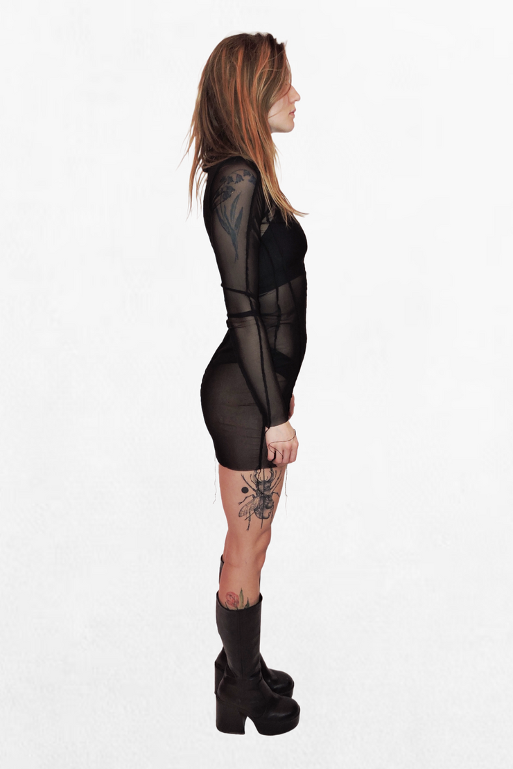  Model wearing a black mesh mini dress that fits snugly against the body. The sheer fabric reveals the silhouette underneath, while the long sleeves add an elegant contrast to the short hemline.