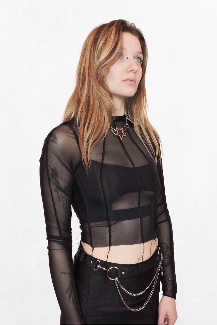  Model wearing a black mesh top with long sleeves and a paneled design. The fabric is fully see-through, creating a bold, layered look that’s perfect for styling over lingerie or under edgy outerwear.