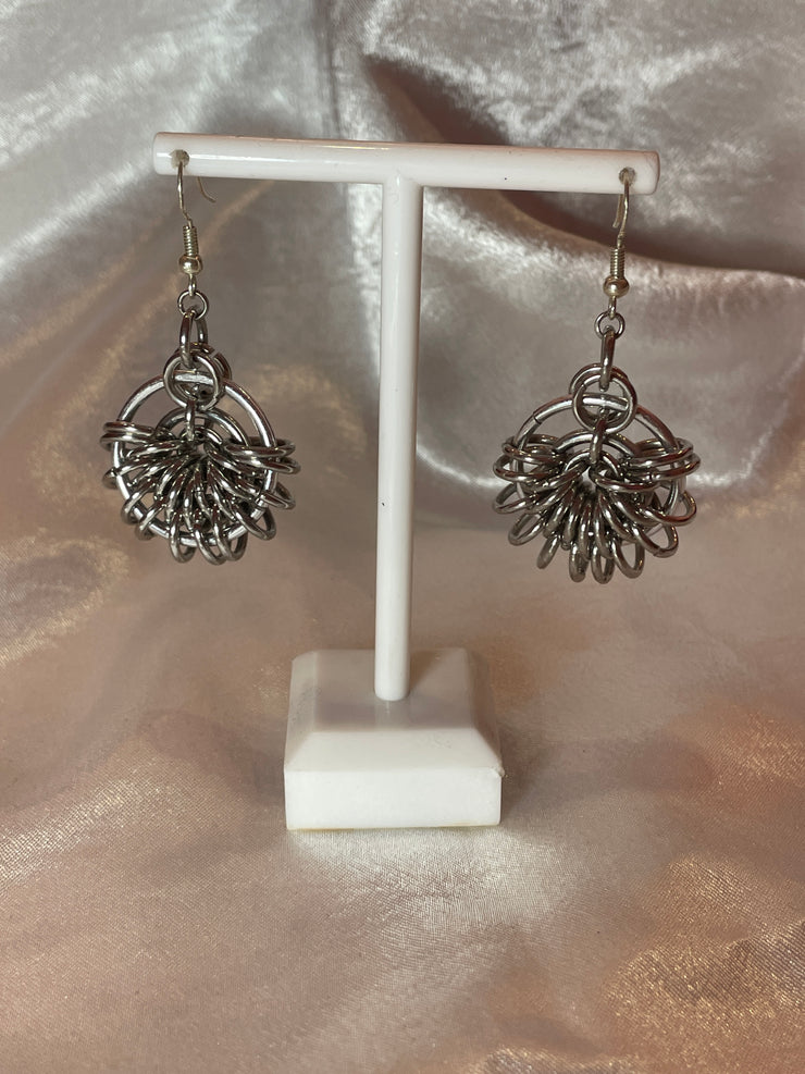 A detailed shot of round silver chain mail earrings, showcasing their unique and intricate design. The earrings hang elegantly, catching the light against a simple, neutral background.